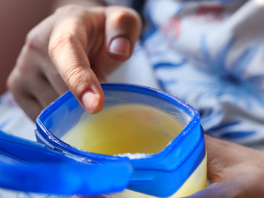 An open plastic pot of Petroleum Jelly with a hand ready to insert a finger into the jelly